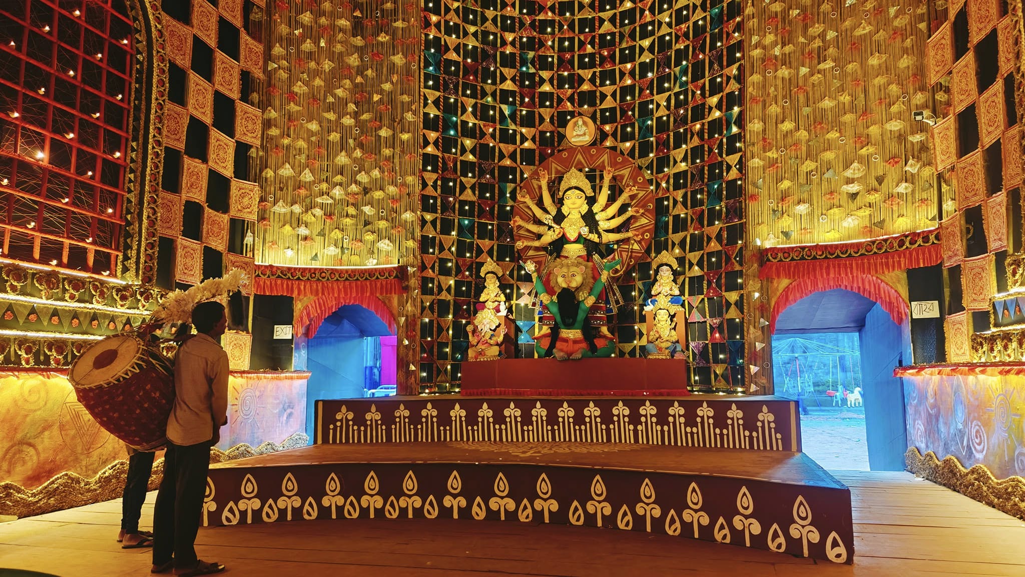 Goddess Durga idol with accompanying deities inside the decorated pandal, dhaki in foreground